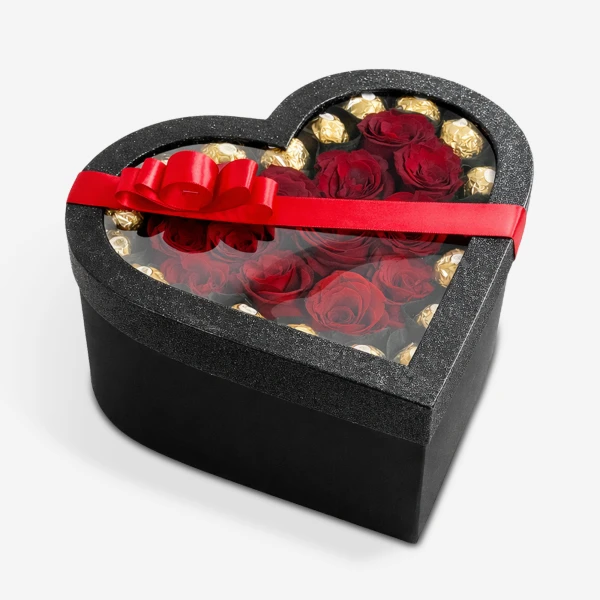 Heart-shaped black box with red roses and gold-wrapped chocolates, tied with a red ribbon.