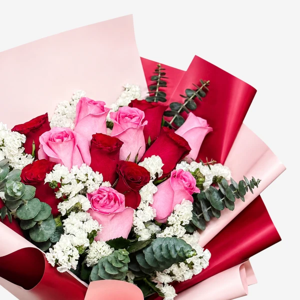 A bouquet of red and pink roses with white statice and eucalyptus, wrapped in pink and red paper.