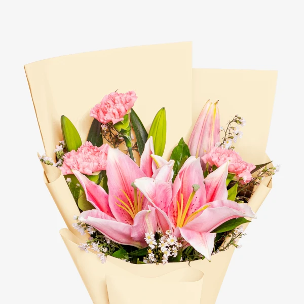 A bouquet of pink lilies and carnations in pale yellow paper wrapping.