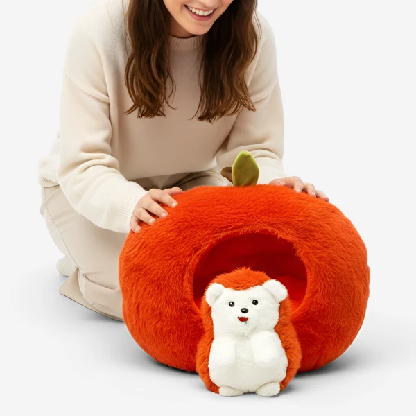 A woman kneels beside an apple-shaped plush bed for a hedgehog toy.