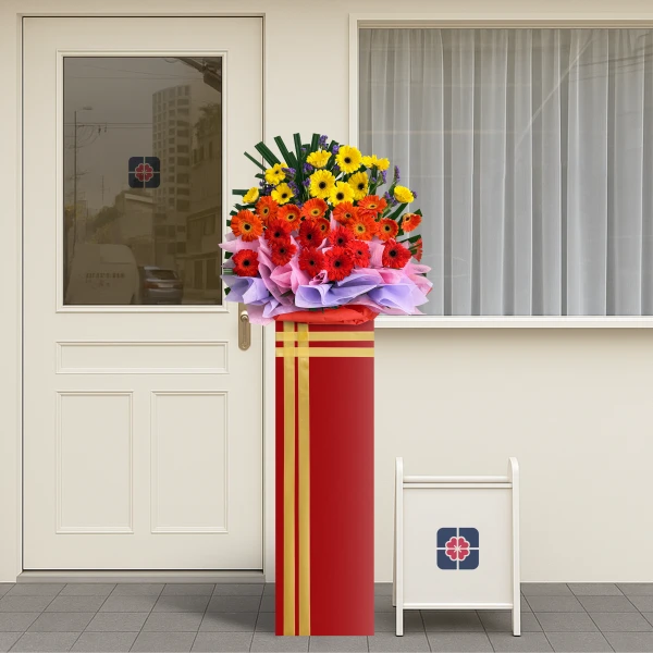 A red flower stand with a vibrant bouquet of orange, red, and yellow gerbera daisies with purple and pink wrapping.