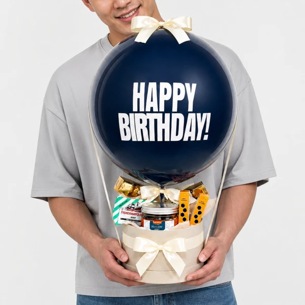 Man holding a balloon that says "Happy Birthday" with a gift box of snacks below.