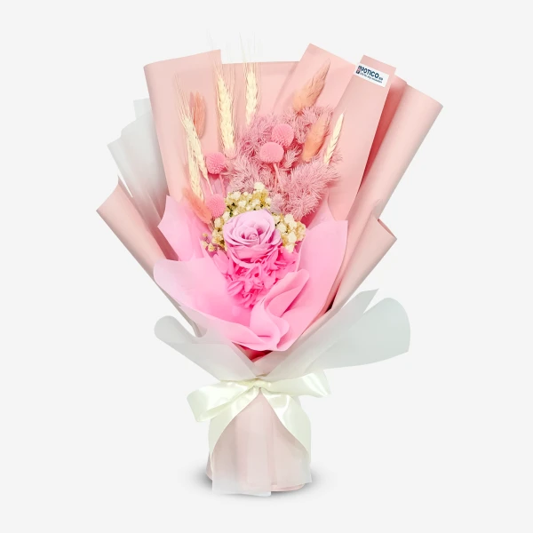 Pink preserved rose bouquet with dried flowers and wheat, wrapped in pink paper and tied with a white ribbon.