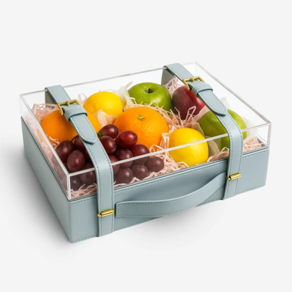 Fruit box with grapes, red apple, oranges, lemons, and green apples, in a blue leather case with a clear lid.