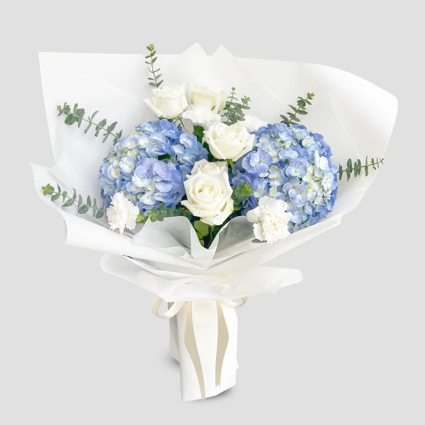 Blue hydrangeas and white roses in a white bouquet with eucalyptus and a ribbon.