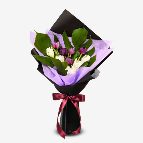 Bouquet of white and violet tulips with dark green leaves, wrapped in black and purple paper and tied with a red ribbon.