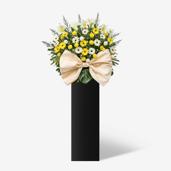 Yellow and white flowers with a large tan bow on a black stand.