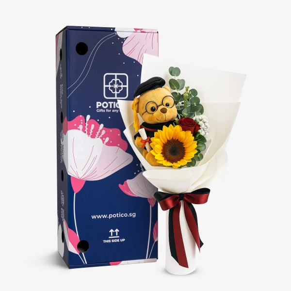 Graduation teddy bear with sunflower and rose bouquet next to a blue gift box.