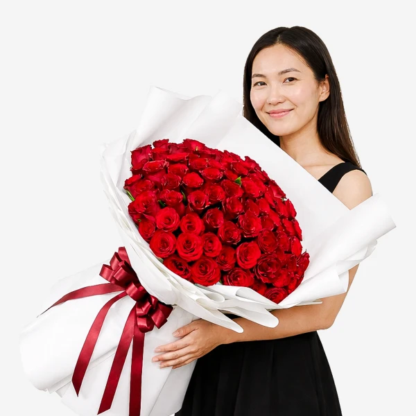A woman smiles holding a large bouquet of 99 red roses wrapped in white paper and tied with a red ribbon.