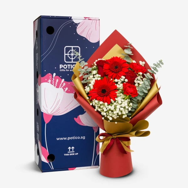 Red gerberas, roses, and carnations in a red and gold bouquet next to a blue patterned gift box.