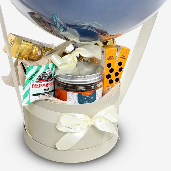 Gift basket with a balloon, candy, jar, and ribbon in a round box.