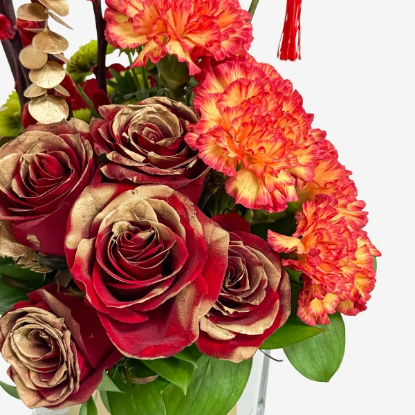 Red roses with gold edges and orange carnations in a vase.