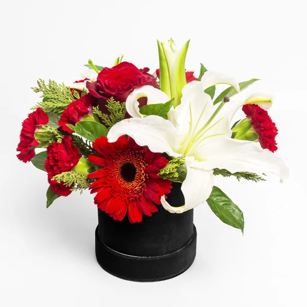Red flowers, including roses, carnations, gerberas, and white lilies, arranged in a black round box.