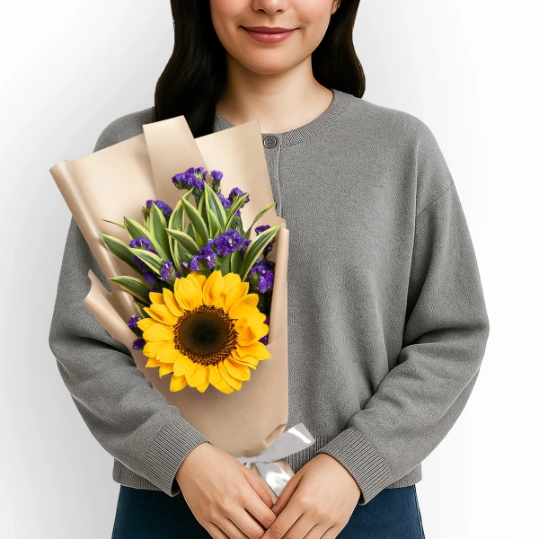 Woman in grey sweater holds a bouquet with a sunflower, violet statice, and green leaves.