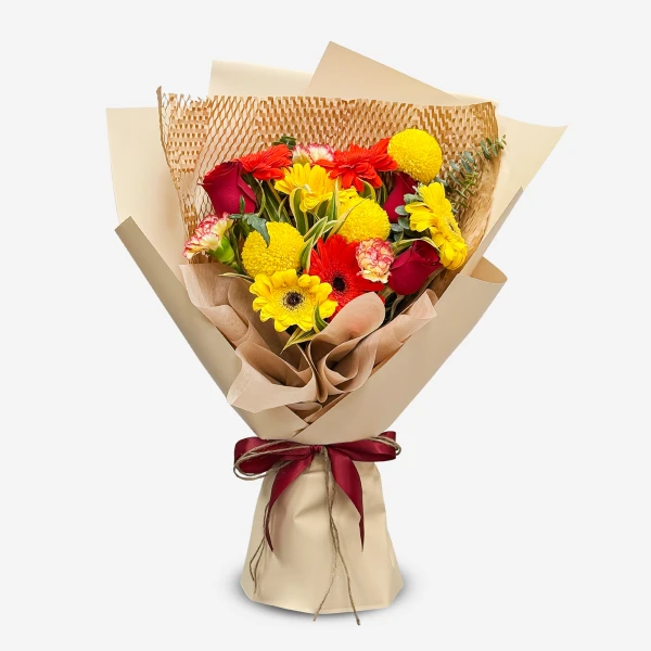 A vibrant bouquet of red roses, yellow gerbera daisies, and red carnations, wrapped in brown paper and tied with a red ribbon.