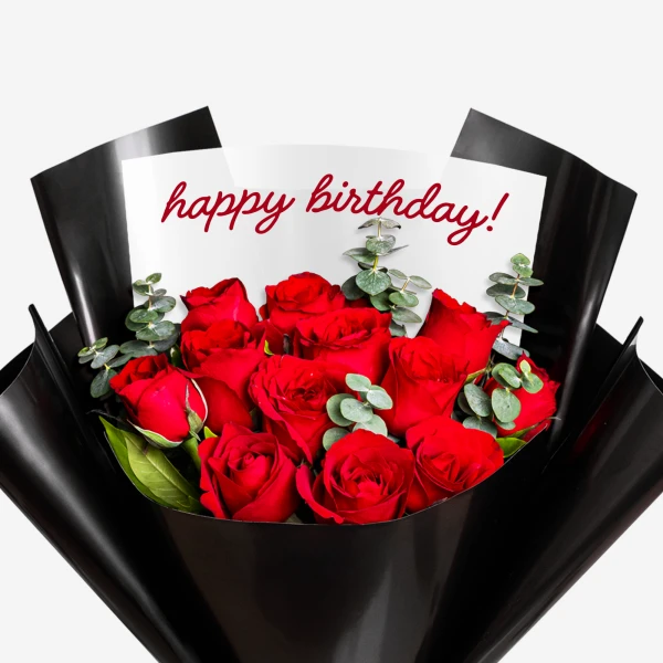 A bouquet of 12 red roses with eucalyptus, wrapped in black paper, with "happy birthday!" written on a card.