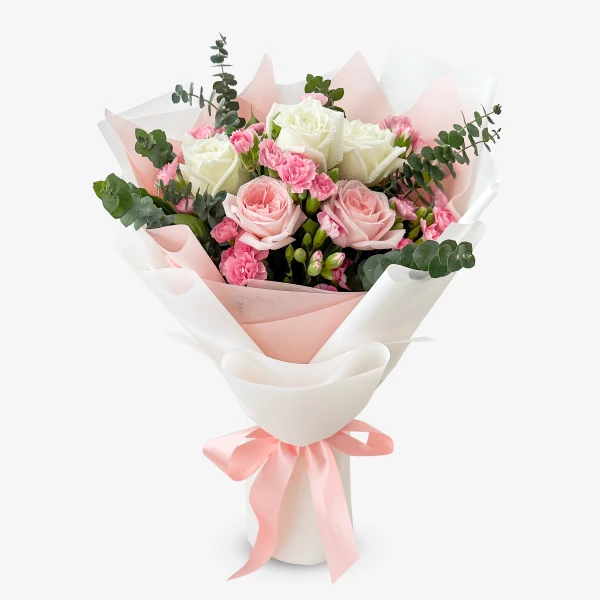 A bouquet of pink and white roses, pink carnations, and eucalyptus, wrapped in white and pink paper with a pink ribbon.
