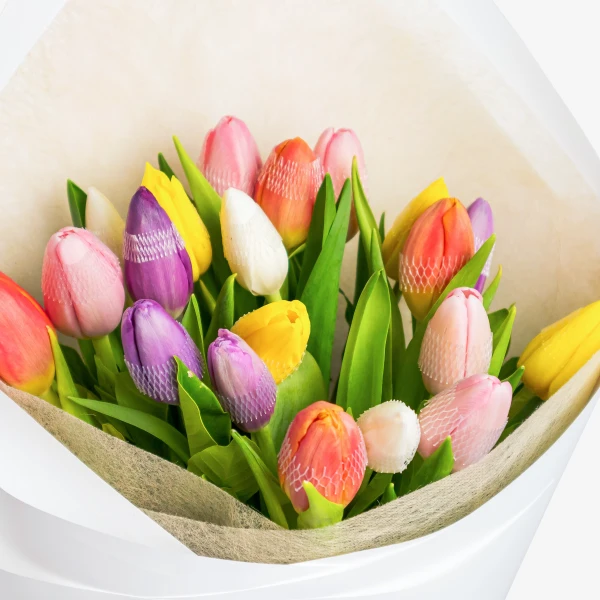 A bouquet of colorful tulips in various shades of pink, yellow, purple, white, and orange, wrapped in white paper.