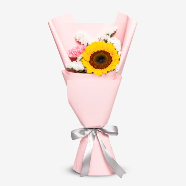 A bouquet featuring a bright sunflower, pink carnations, and white filler flowers, wrapped in pink paper and tied with a silver ribbon.