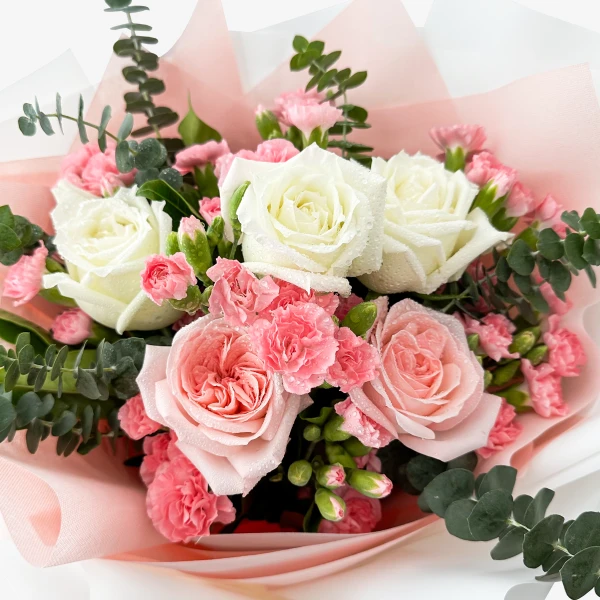 Bouquet of white and pink roses with pink carnations and eucalyptus, wrapped in pink paper.