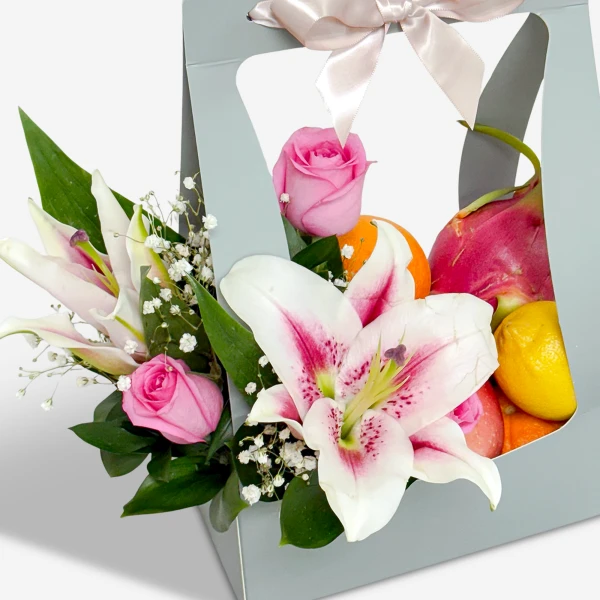 A gift box filled with pink roses, white lilies, dragon fruit, oranges, and lemons.