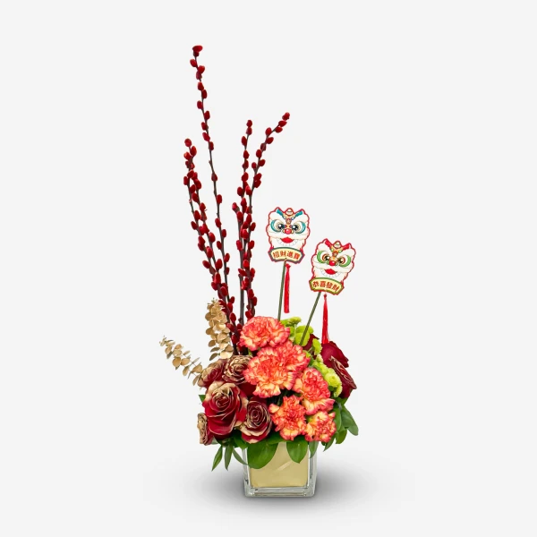A floral arrangement with red pussy willow branches, red and orange carnations, red roses, and two lion dance decorations in a glass vase.