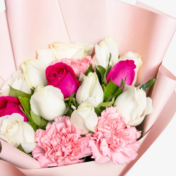 A bouquet of pink carnations and white and pink roses wrapped in pink paper.