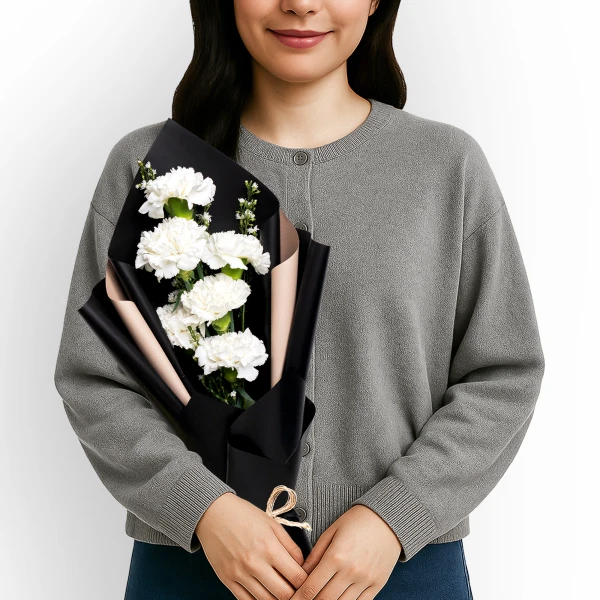 Woman in gray cardigan holding a bouquet of white carnations wrapped in black paper.