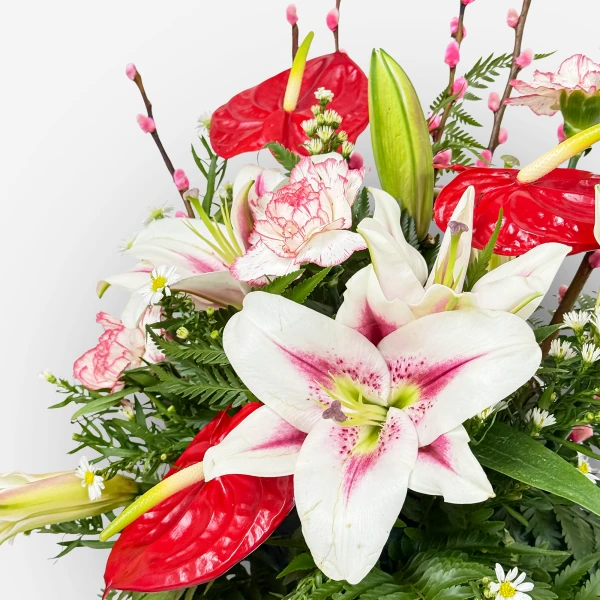 White lilies and red anthuriums with pink accents and greenery in a bouquet.