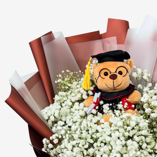 Graduation teddy bear in a bouquet of baby's breath, wearing a cap and gown.