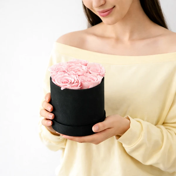 Woman holding black box of preserved pink roses.