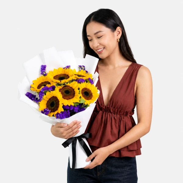 Woman holding a bouquet of sunflowers and purple statice flowers.