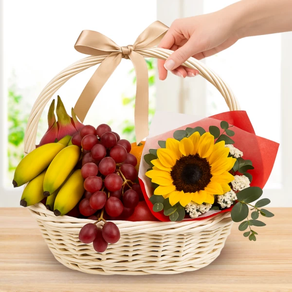 Wicker fruit basket with dragonfruit, bananas, grapes, orange, apple, and a sunflower.