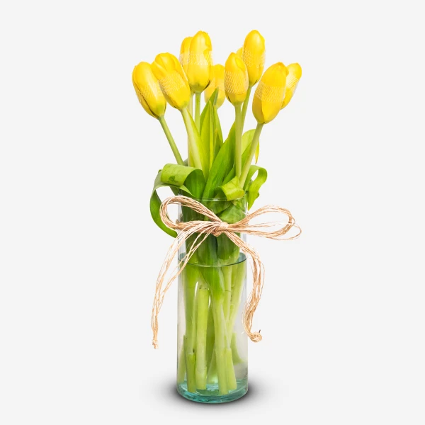 Yellow tulips tied with twine in a glass vase, against a white background.