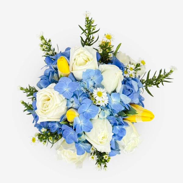 White roses, blue hydrangeas, yellow tulips, and daisies in a bouquet.
