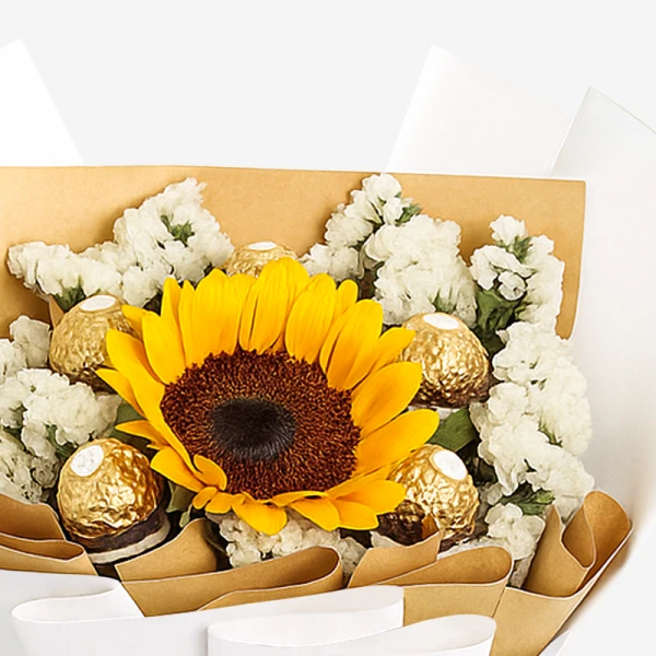 Sunflower with white flowers and gold-wrapped chocolates in a brown and white bouquet.
