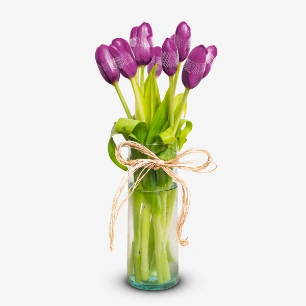 Violet tulips arranged in a clear glass vase, tied with a straw bow.