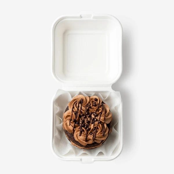Chocolate cake with chocolate frosting and sprinkles in a white takeout box.