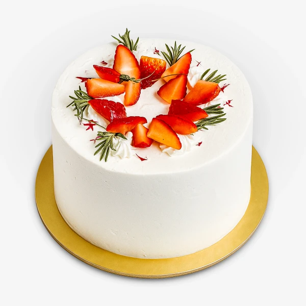 White frosting cake topped with sliced strawberries and rosemary sprigs on a gold cake board.