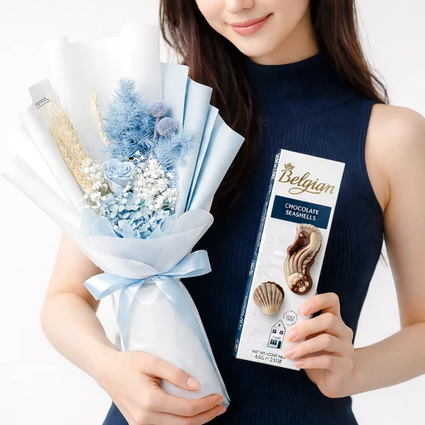 Woman holds a blue dried flower bouquet and a box of Belgian chocolate seashells.