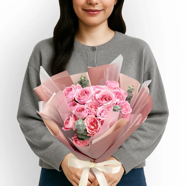 Woman holding a pink spray rose and eucalyptus bouquet with a cream ribbon.