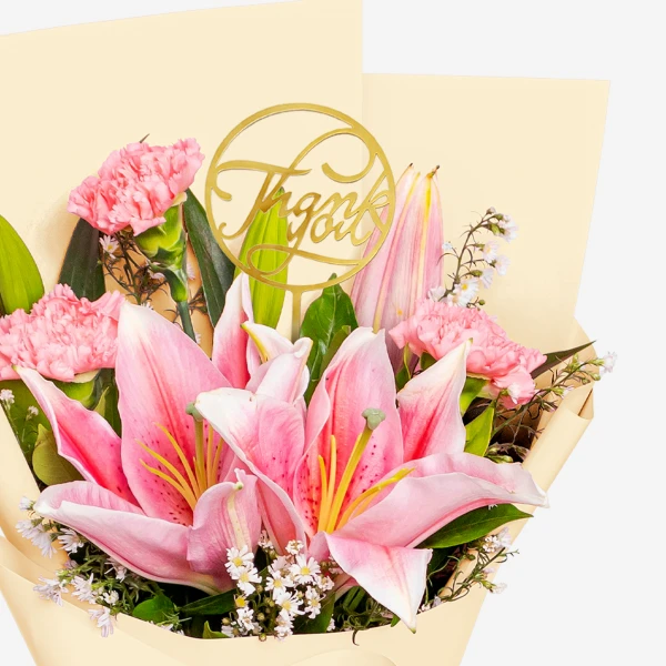 Pink lilies and carnations arranged in a bouquet with a gold "thank you" pick.