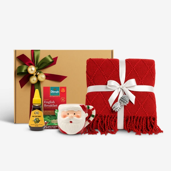 Christmas gift box with tea, honey, Santa mug, and red blanket with white ribbon and pinecones.