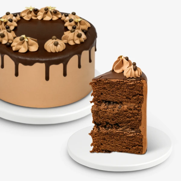 Chocolate birthday cake with chocolate frosting, drips, and whipped cream swirls, next to a slice.