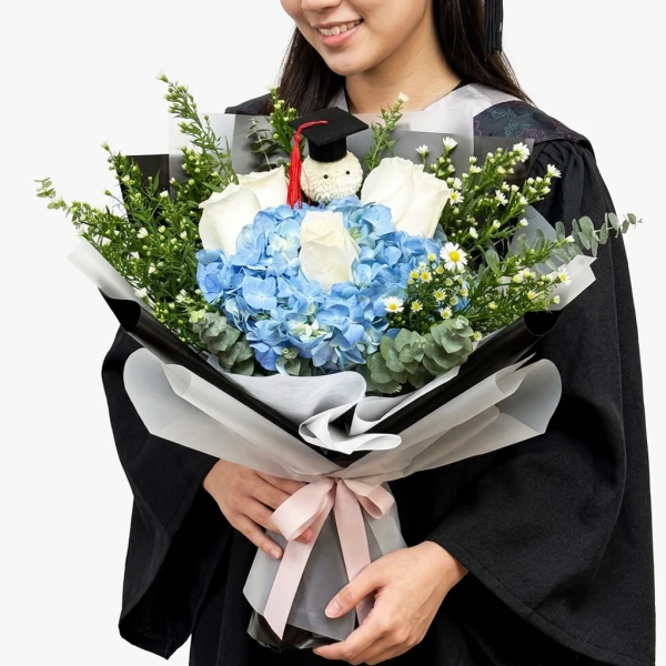 Graduation bouquet with blue hydrangea, white roses, baby's breath, and a graduation cap charm.