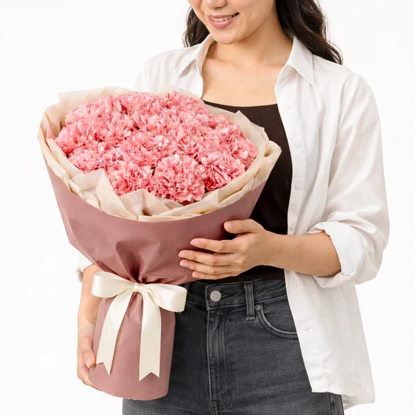 A person holding a bouquet of 60 pink carnations wrapped in blush paper with a white ribbon.