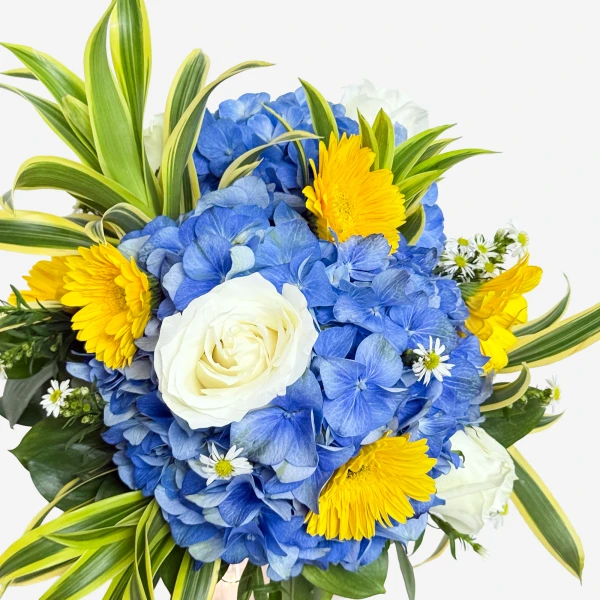 A bouquet of blue hydrangeas, yellow gerbera daisies, white roses, and green foliage.
