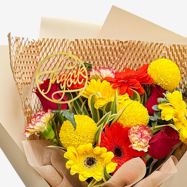 Bright bouquet of red, yellow, and orange flowers with a gold "Thank you" topper.