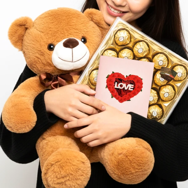 Brown teddy bear holding box of chocolates and card with "LOVE" on it.