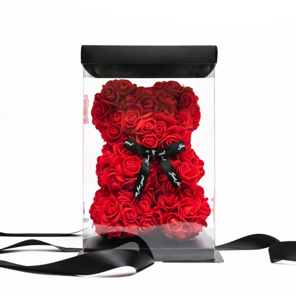 Red rose teddy bear in clear box with black ribbon, on white background.